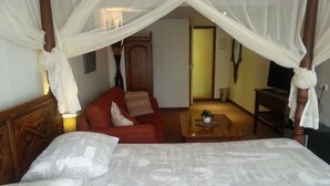 A bedroom with a four-poster bed, a red sofa, and a small table with a plant. - Hotel Den Helder (Den Helder)