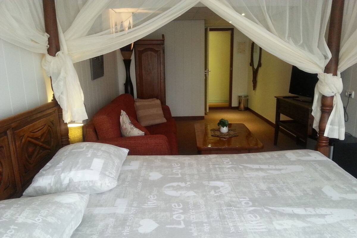 A bedroom with a four-poster bed, a red sofa, and a small table with a plant.