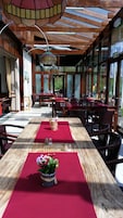 Un restaurante con mesas y sillas de madera, manteles rojos y grandes ventanales con vistas al exterior.