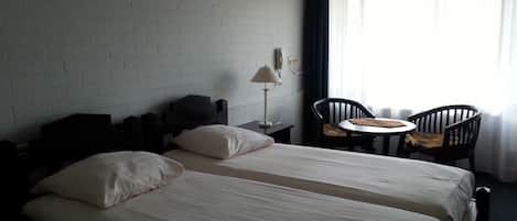 A hotel room with two beds, a small table, two chairs, a lamp, and a window with curtains.