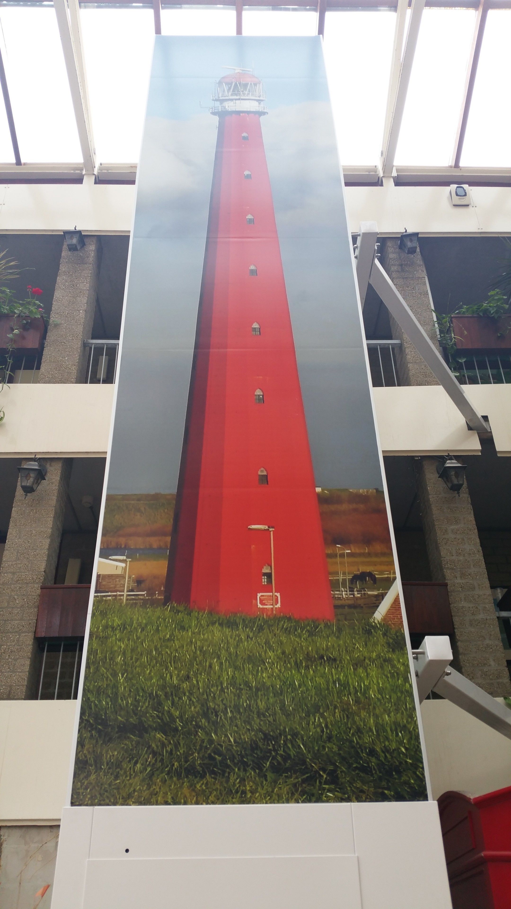Un faro rojo con múltiples ventanales, frente a un edificio con techo de cristal.