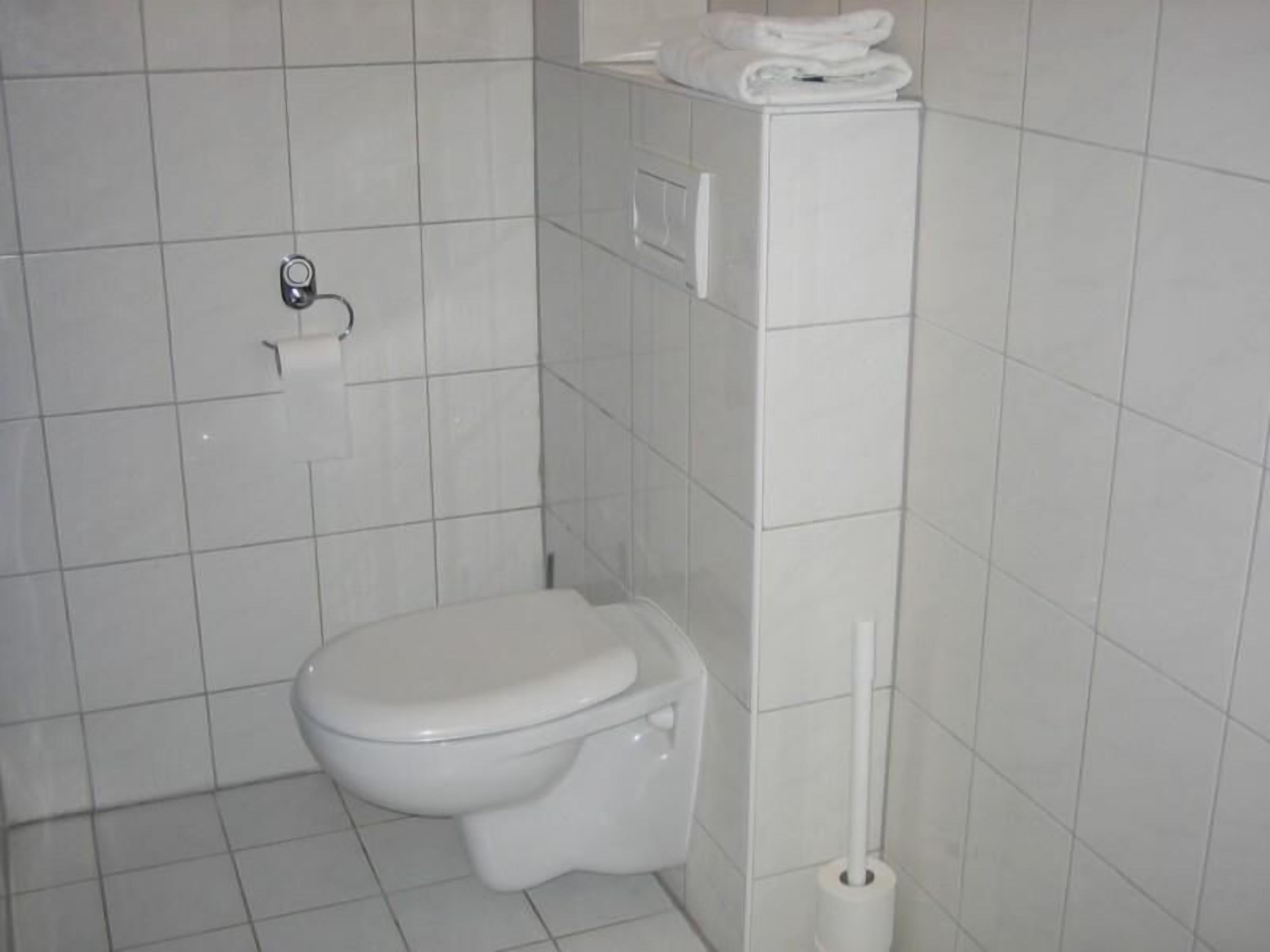A small, white bathroom with a toilet, a toilet paper holder, and a towel rack.