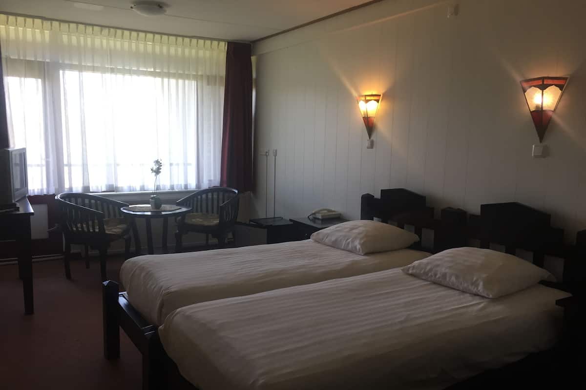 A hotel room with two beds, a desk with a chair, a small table, and two wall-mounted lamps.