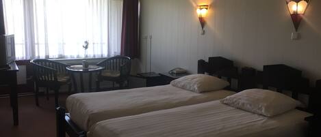 Habitación de hotel con dos camas, un escritorio con una silla, una mesita y dos lámparas fijadas a la pared.