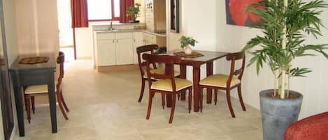 Un coin repas avec une table et des chaises en bois, une plante en pot et une cuisine en arrière-plan.