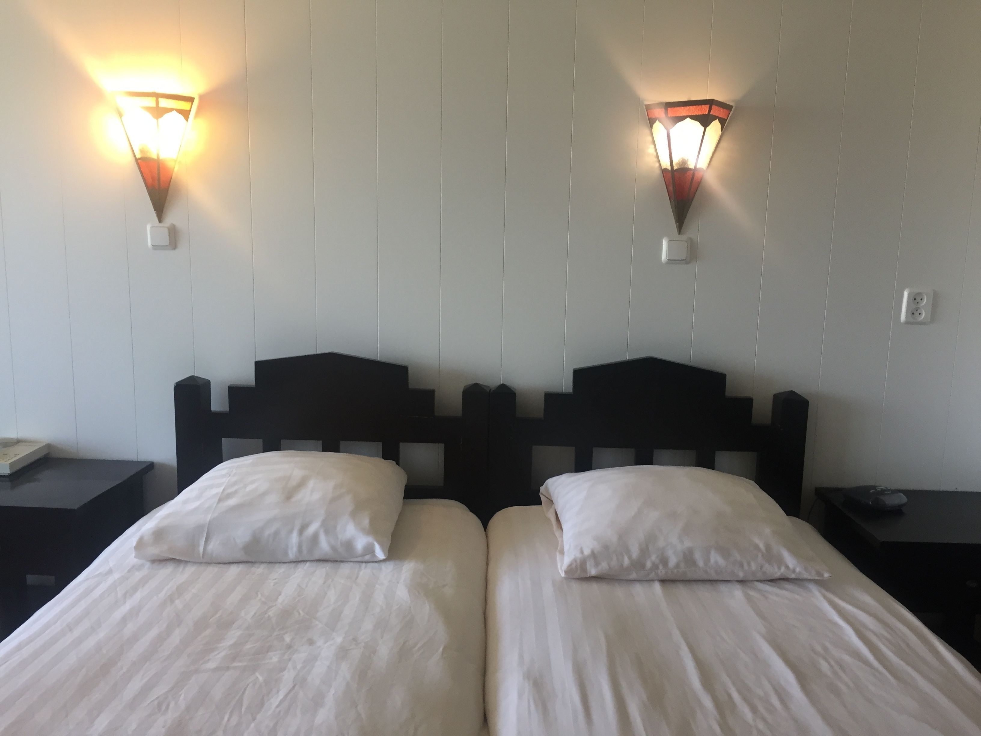 A hotel room with two beds, each with white linens, and two wall-mounted light fixtures.