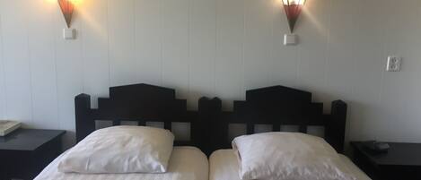 A hotel room with two beds, each with white linens, and two wall-mounted light fixtures.