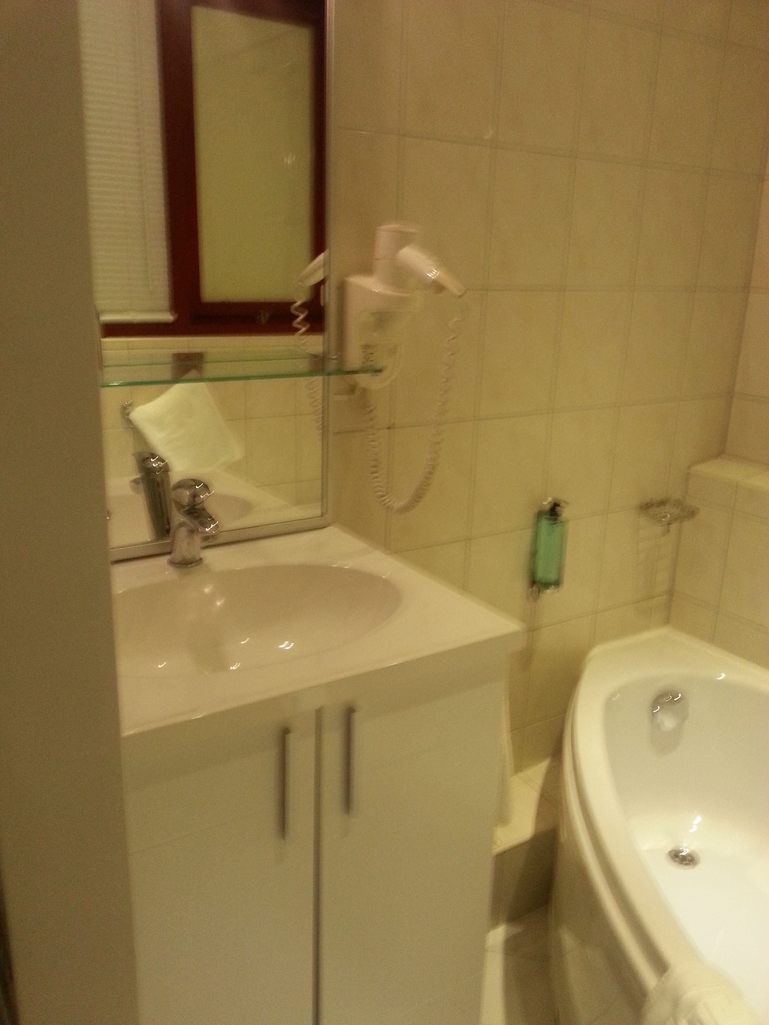 A bathroom with a white sink, a mirror, a hairdryer, and a bathtub.
