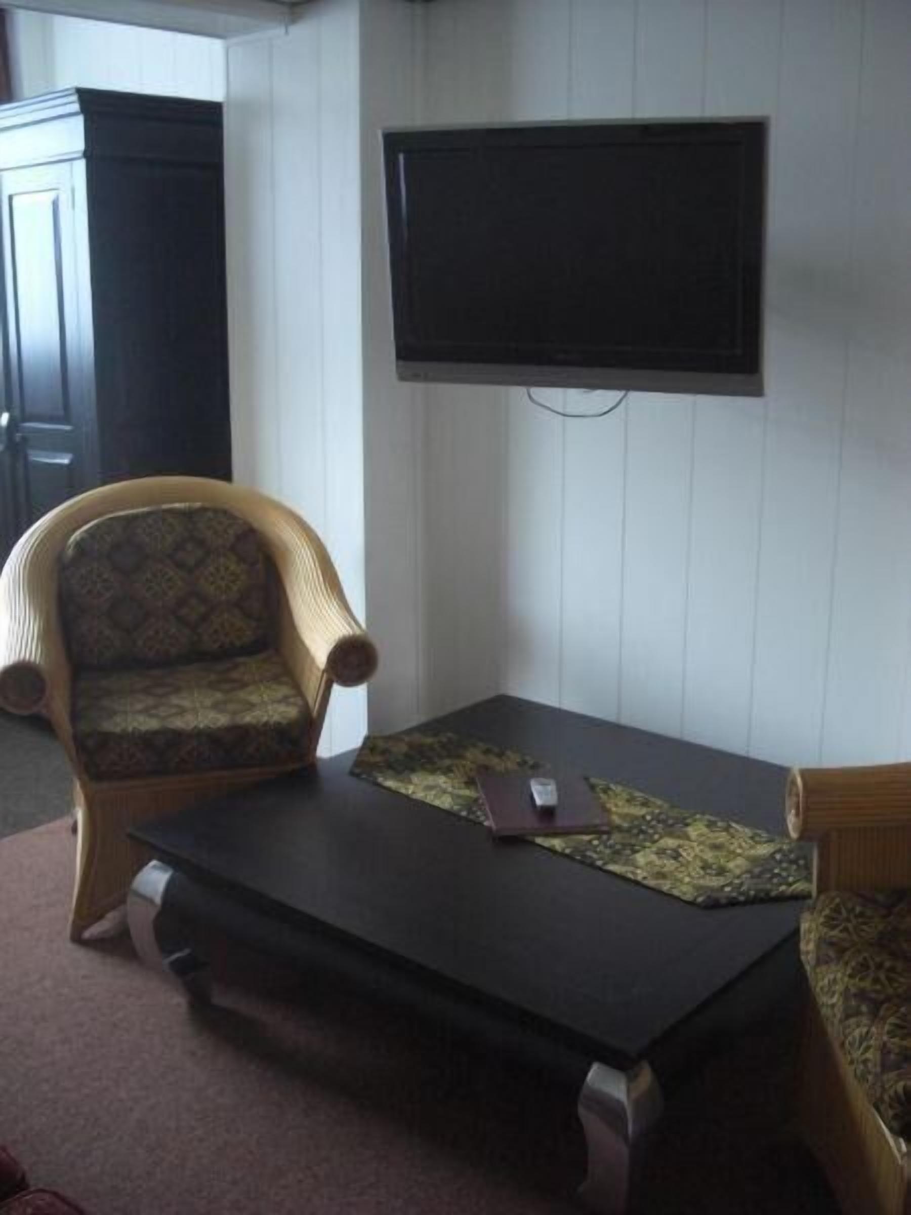 A living room with a dark coffee table, a patterned armchair, and a television mounted on the wall.