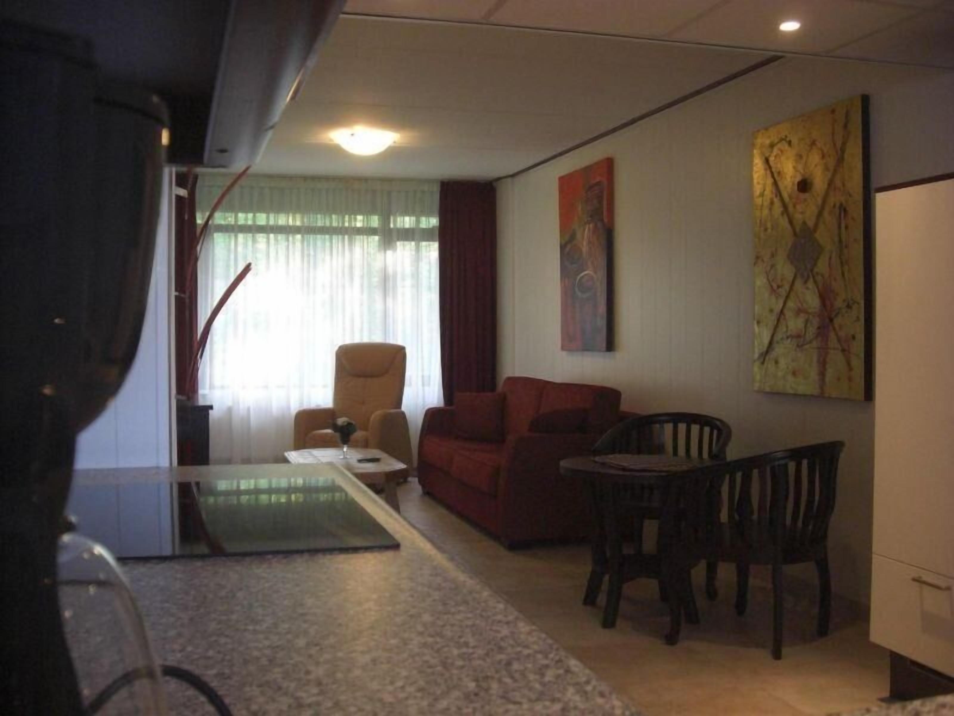 Un espace de vie compact comprenant un canapé, une table à manger avec des chaises et une petite table basse. Deux tableaux ornent le mur, et une fenêtre est agrémentée de rideaux.