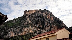 Una fortaleza de piedra histórica sobre una montaña, con un edificio de techo rojo al frente.