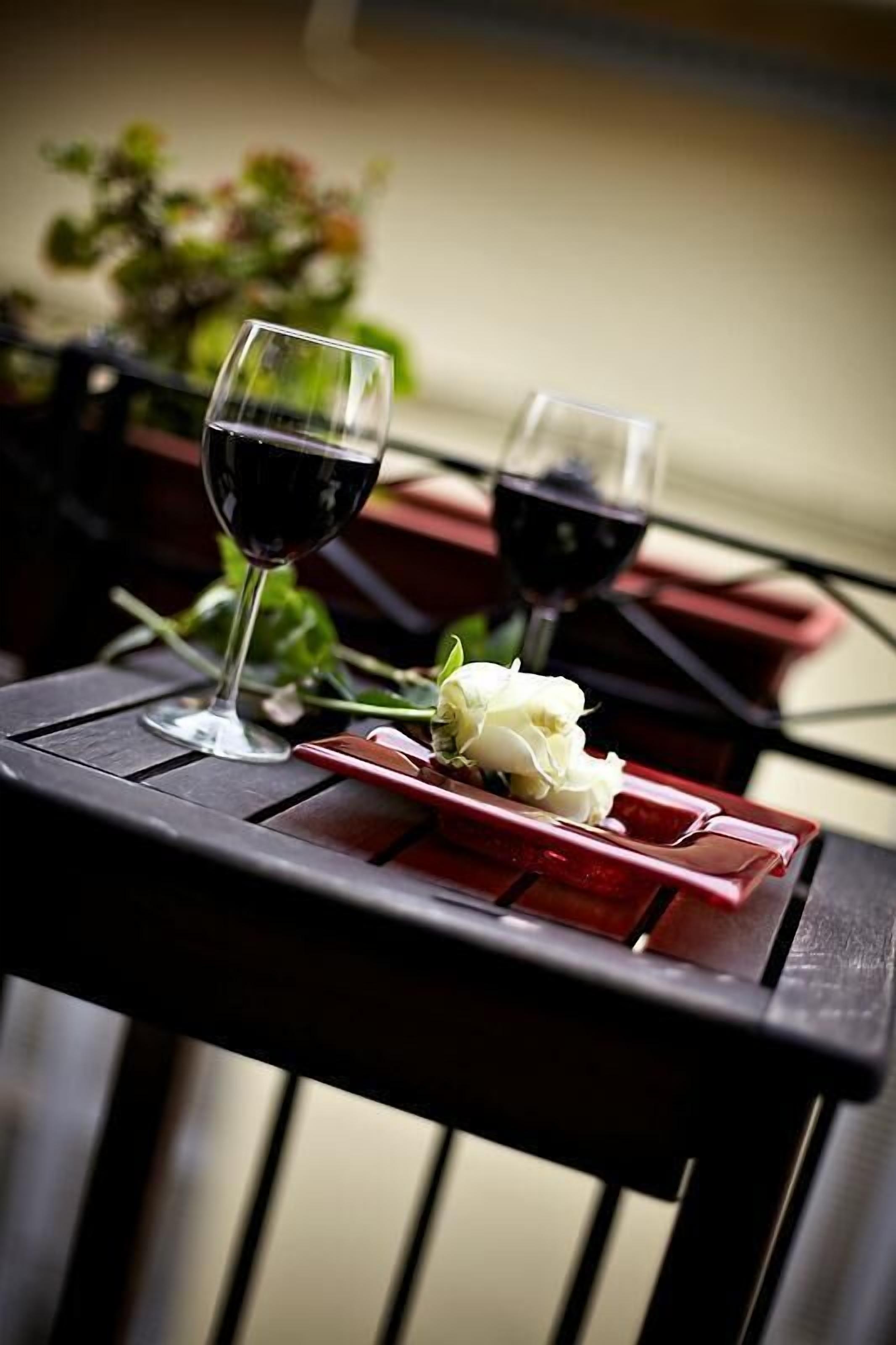 A table with two wine glasses and a white rose on a red tray.