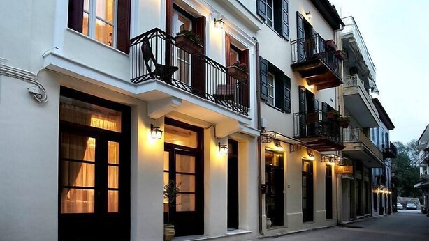 Una hilera de edificios blancos con contraventanas negras y balcones, con ventanas y puertas iluminadas, que sugieren una calle tranquila al anochecer.