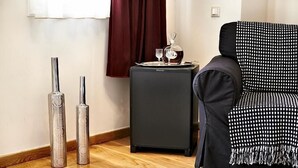 Una habitación con un sofá negro, una mesita auxiliar pequeña de color negro con una bandeja que sostiene vasos y una botella, y dos jarrones altos y transparentes.