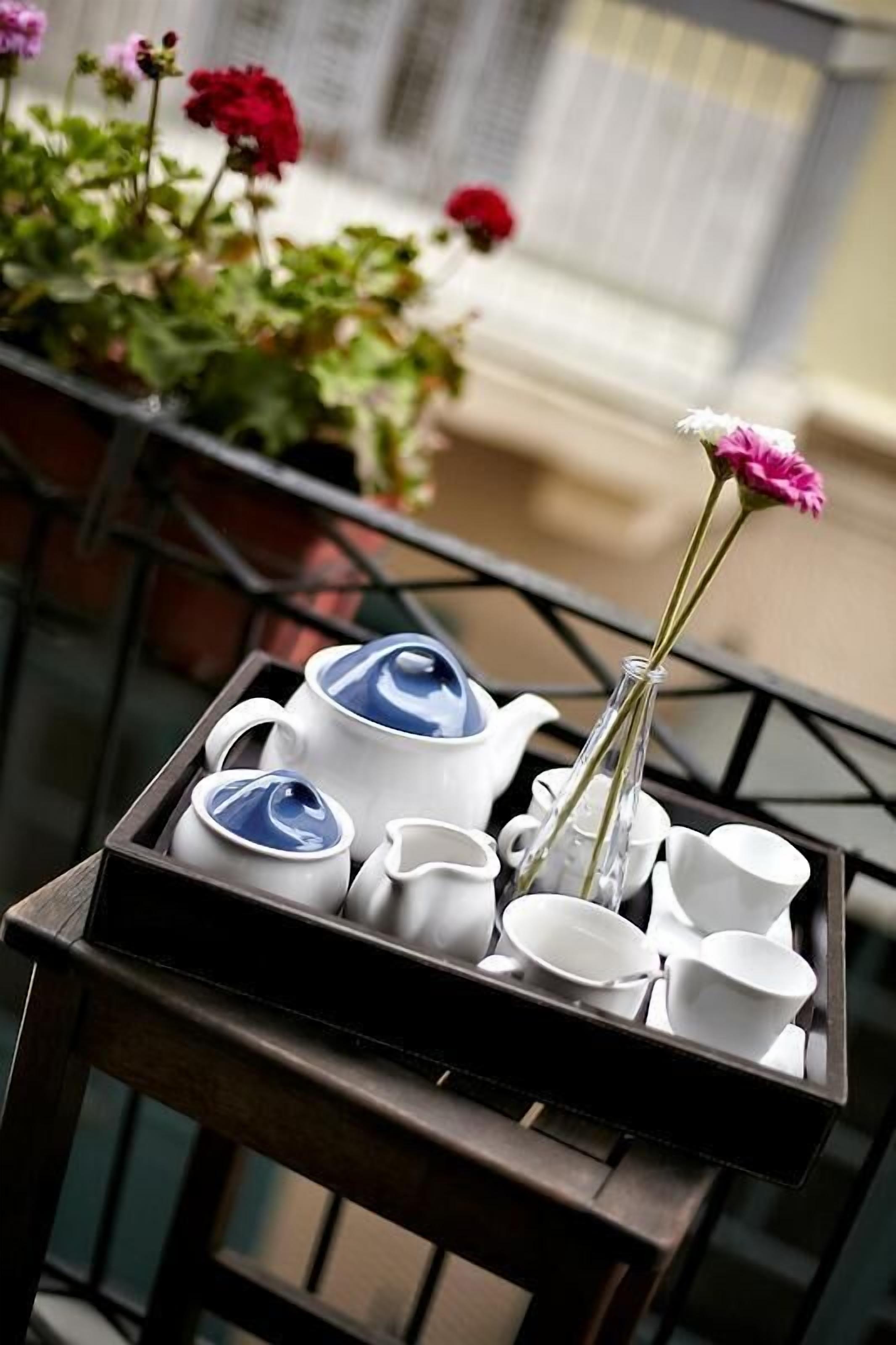 A tray with a teapot, cups, and a vase with flowers on a balcony.