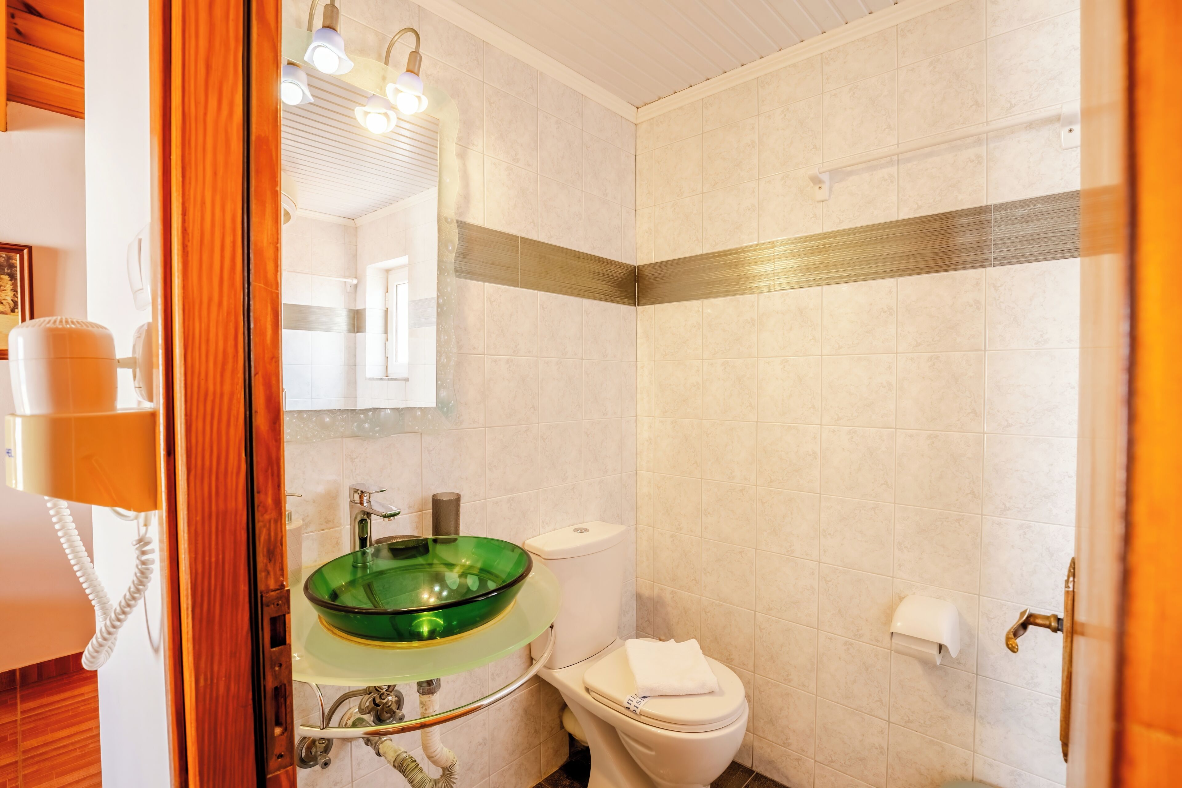 A bathroom with a glass sink, toilet, and a mirror.