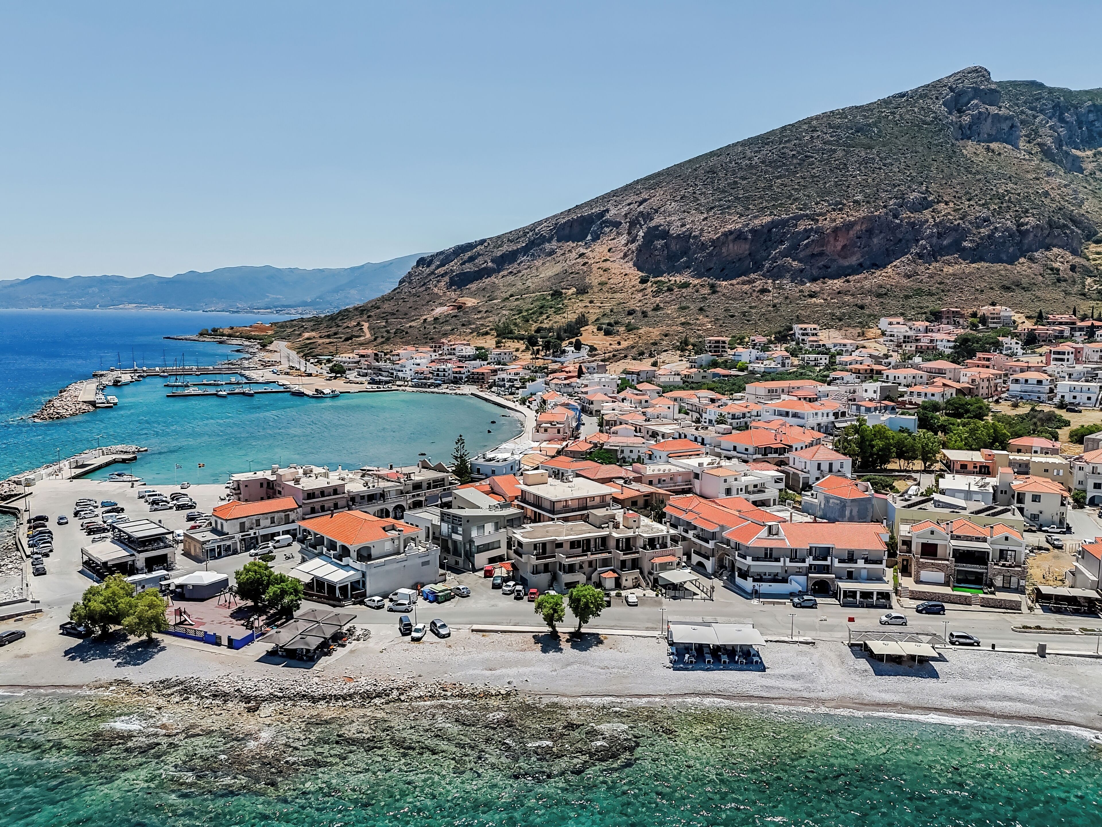 Un pueblo costero con un puerto deportivo, aguas azul cristalino y edificios de techos rojos.