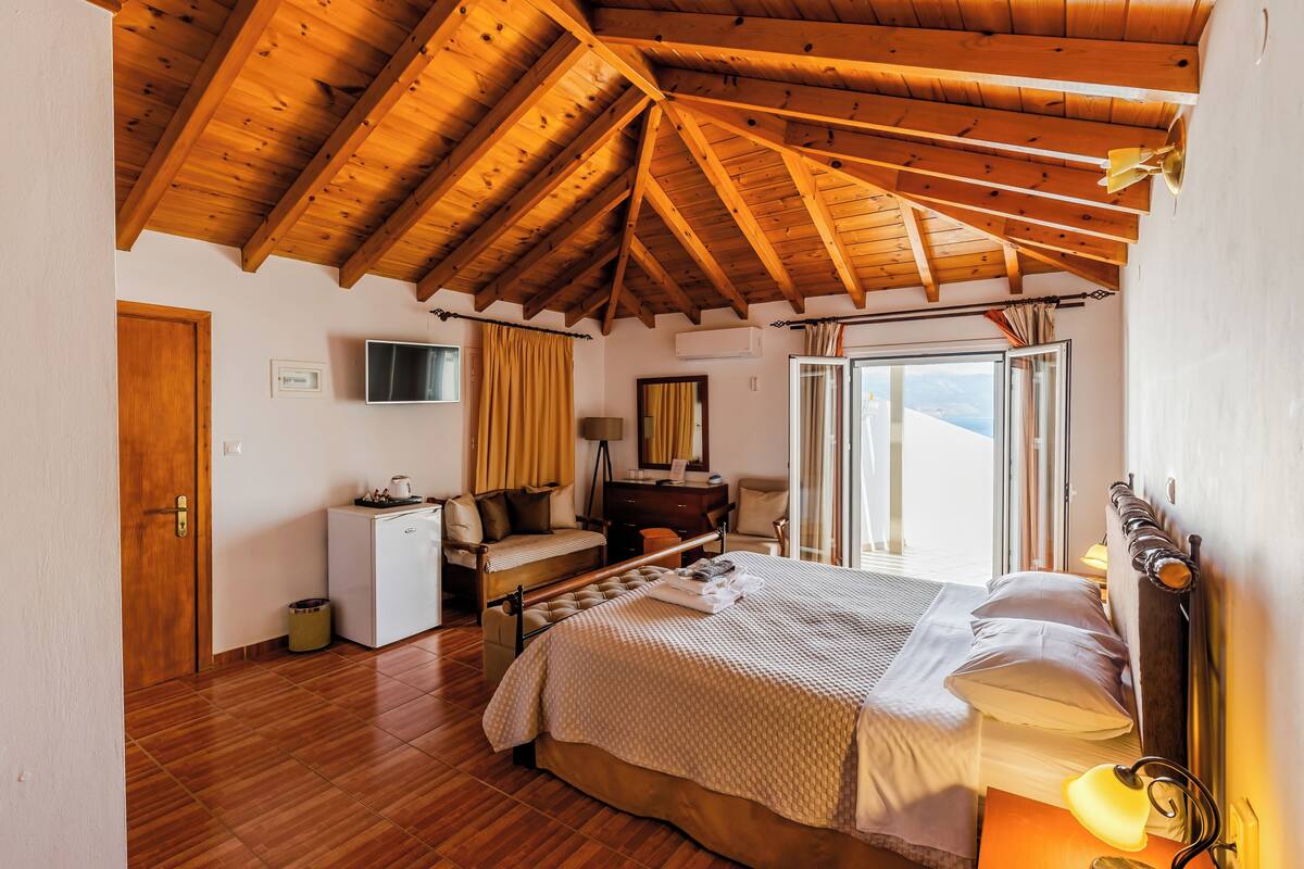 A bedroom with a wooden ceiling, a bed, a desk, a chair, and a window with curtains.
