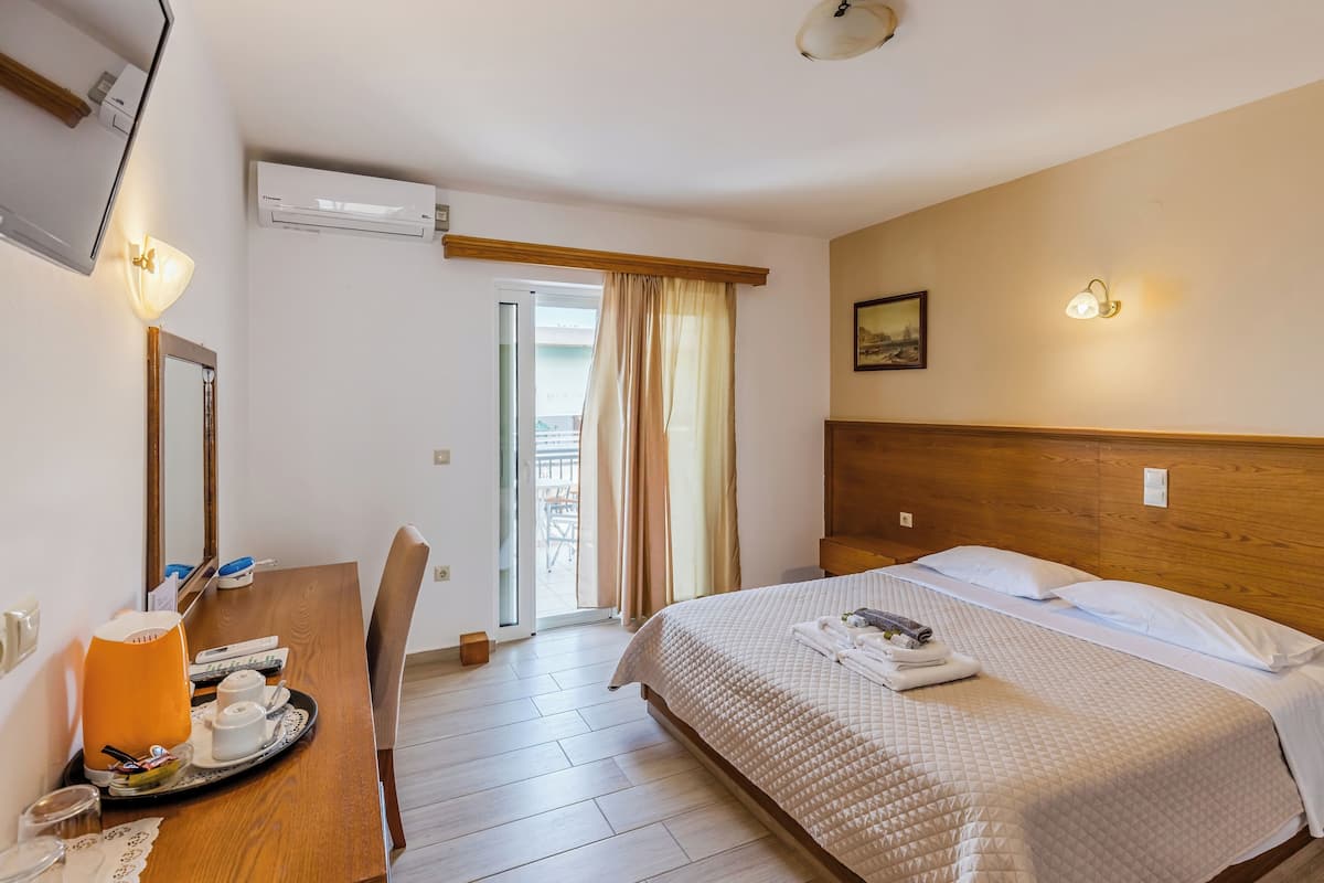 A hotel room with a bed, a desk with a tray of breakfast items, a mirror, and an air conditioning unit.