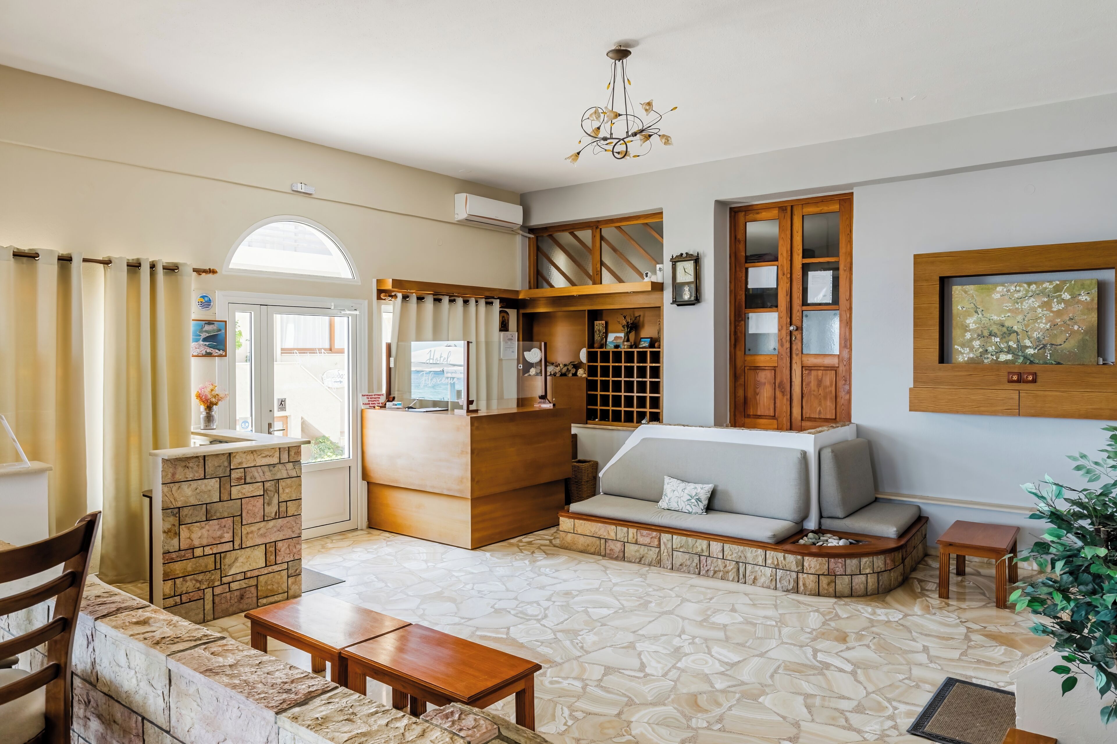 Amplia sala de estar con suelo de piedra, mostrador de recepción de madera, sofá con cojines y televisor.
