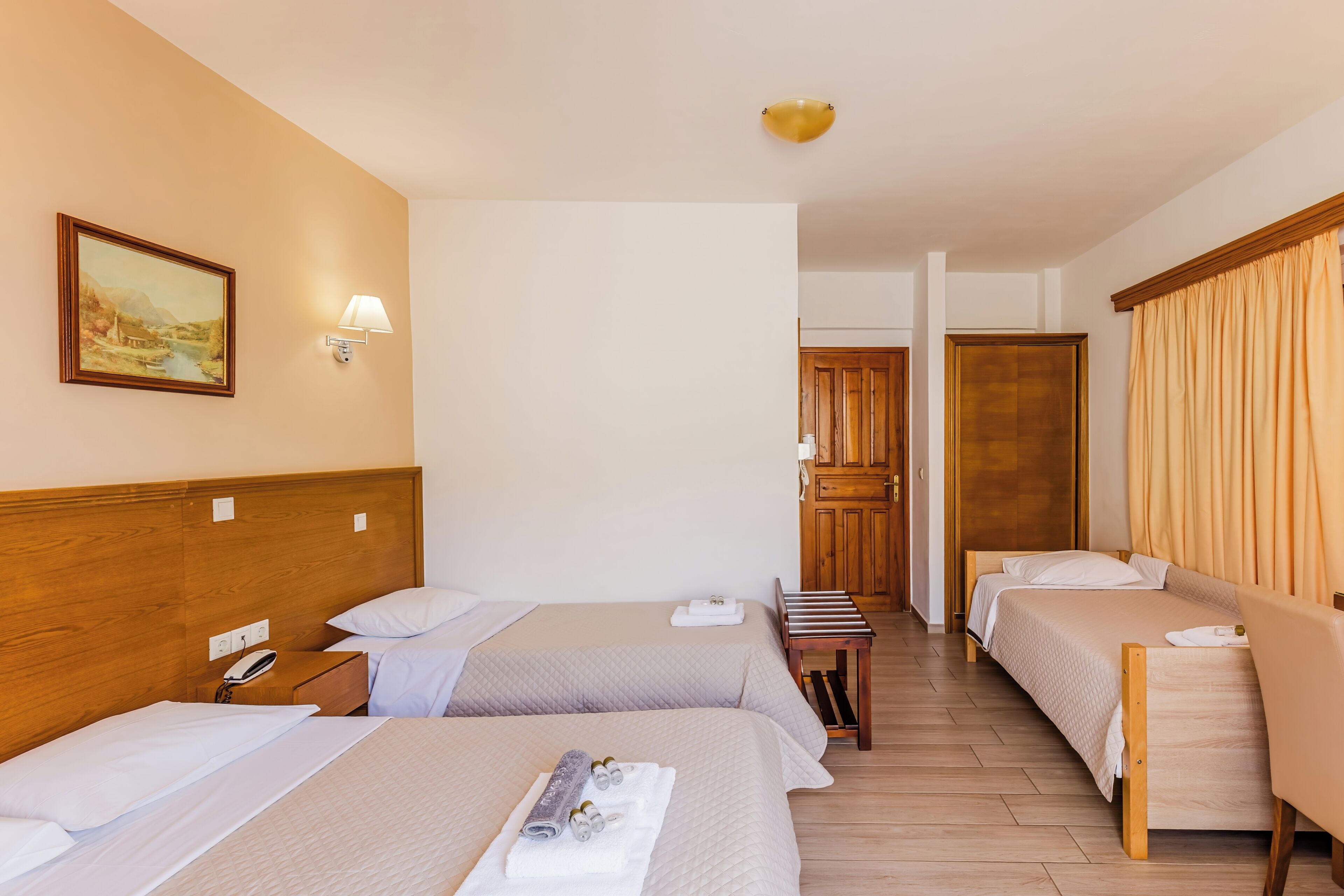 A hotel room with two beds, a wooden headboard, a painting on the wall, a bedside lamp, and a wooden floor.