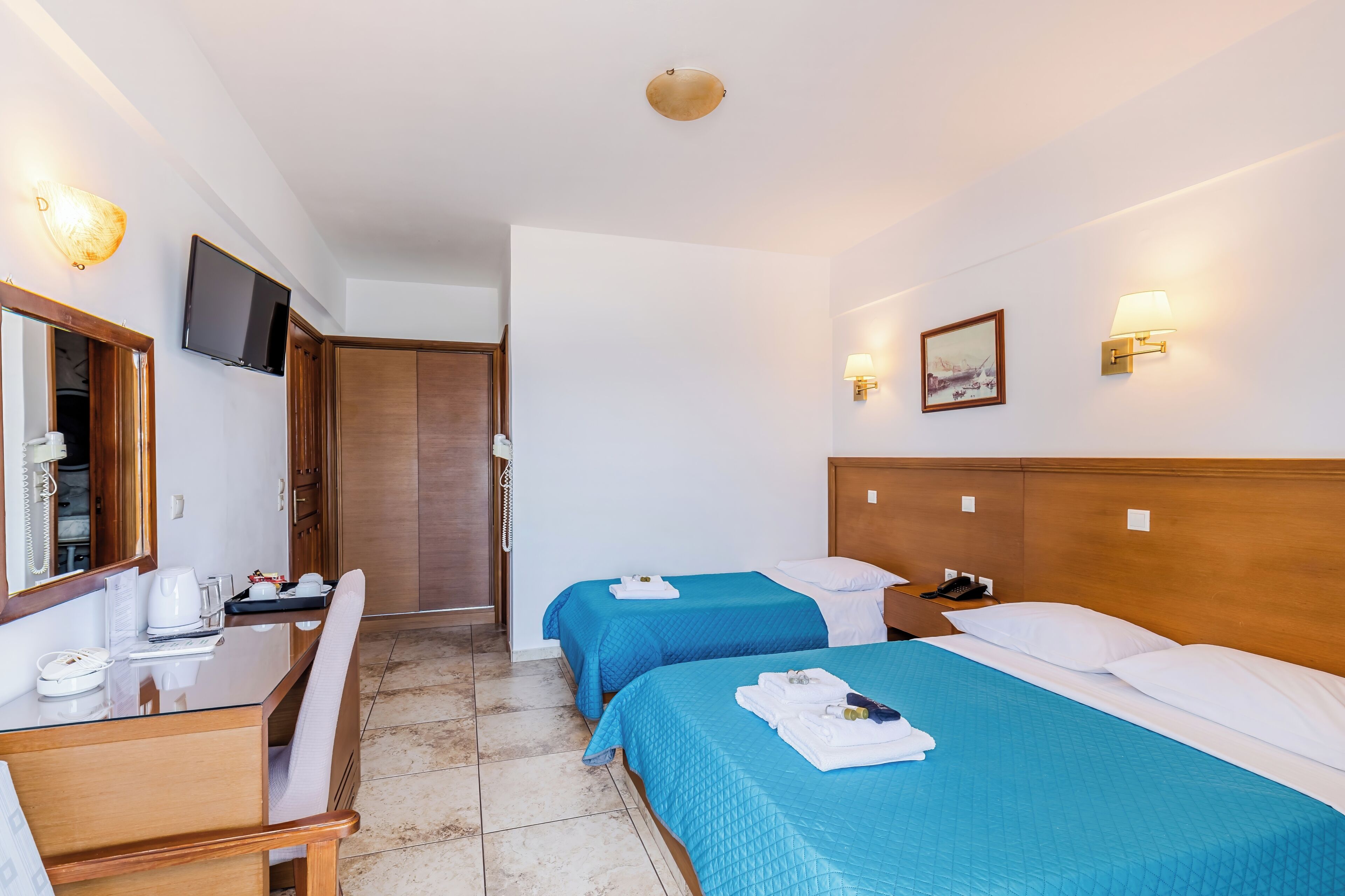 Een hotelkamer met twee bedden, een bureau, een stoel, een televisie en een spiegel.