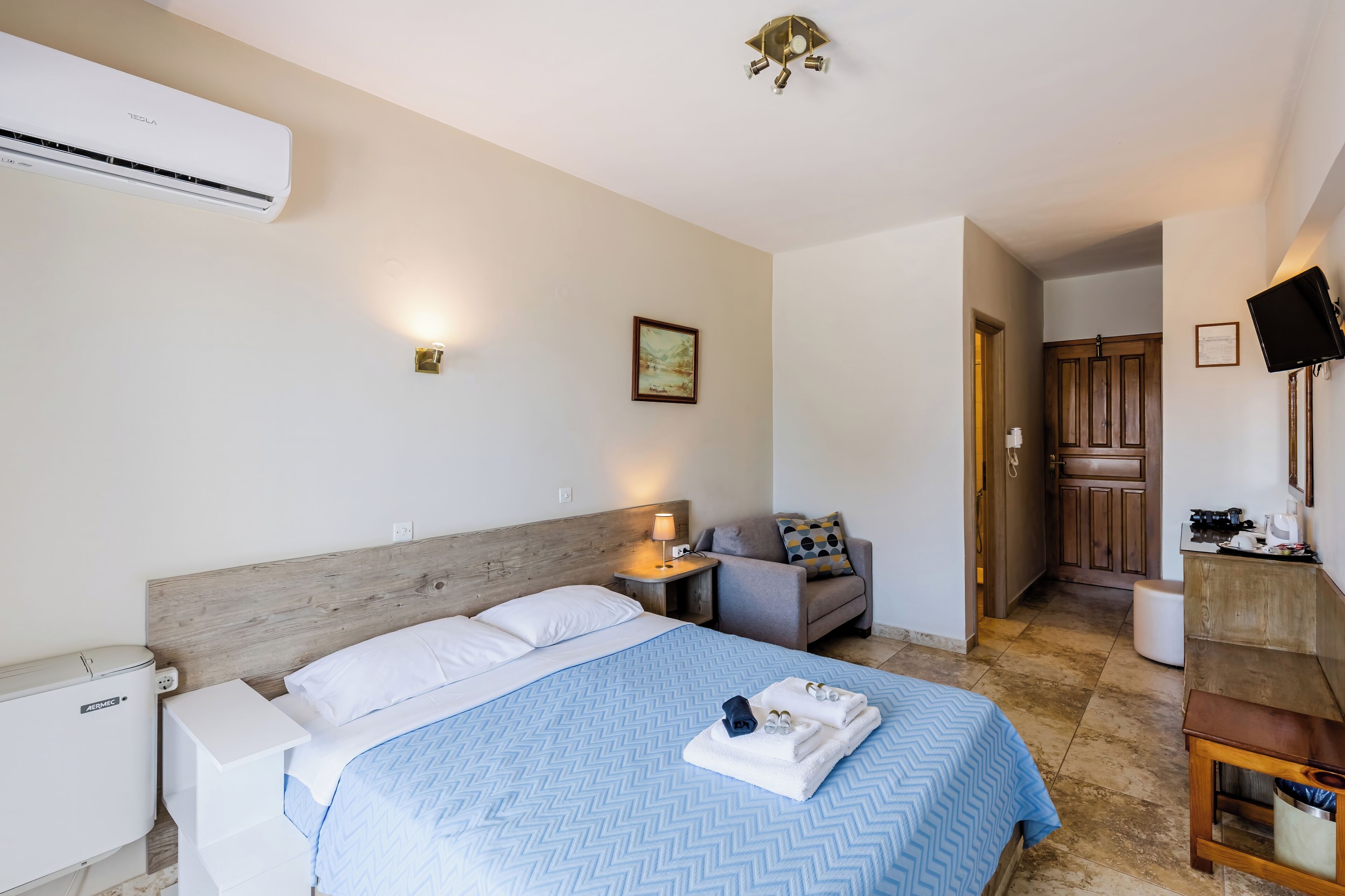 A hotel room with a bed, bedside table, lamp, and a view into the kitchen.
