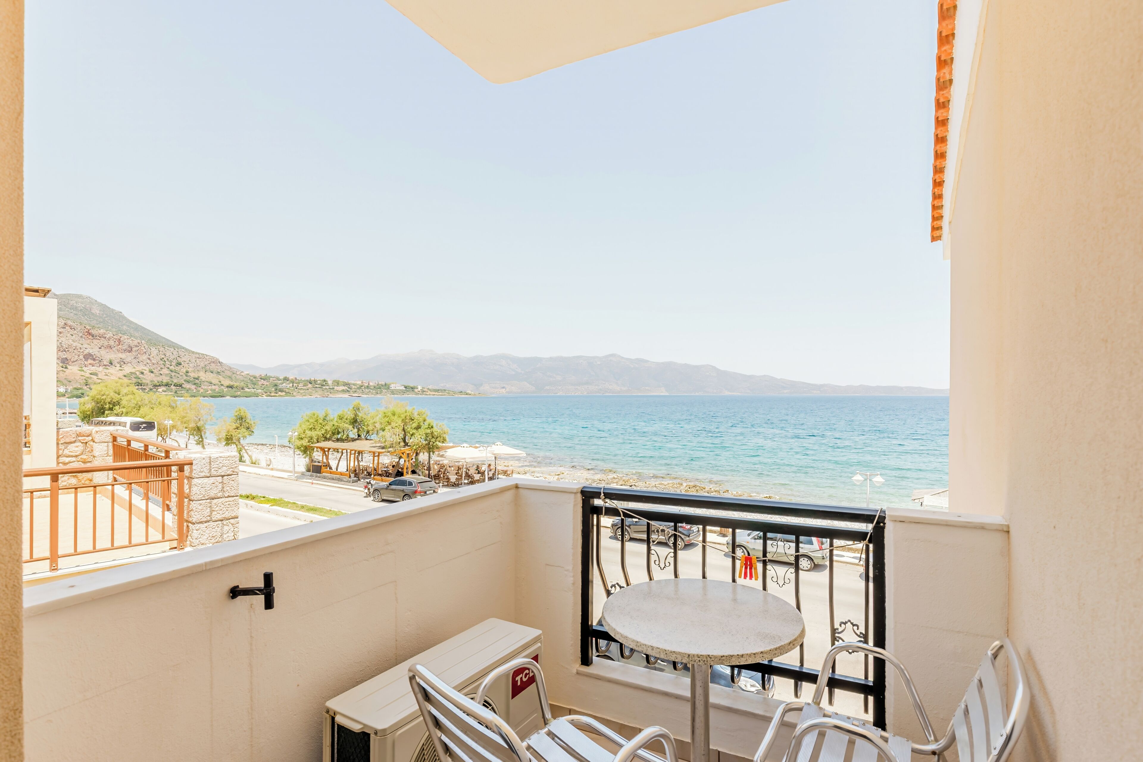 A balcony with a table and chairs, overlooking a beach and sea.