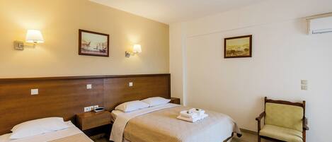 A hotel room with two beds, a chair, and wall-mounted lamps.