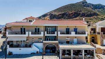 A multi-story hotel with balconies, a covered outdoor seating area, and a mountain backdrop.