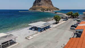 Una carretera costera con una isla rocosa, mar azul cristalino y coches aparcados.