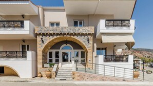 Un edificio de dos pisos con un arco de piedra en la entrada, balcones con barandas de metal y una vista despejada del paisaje circundante.
