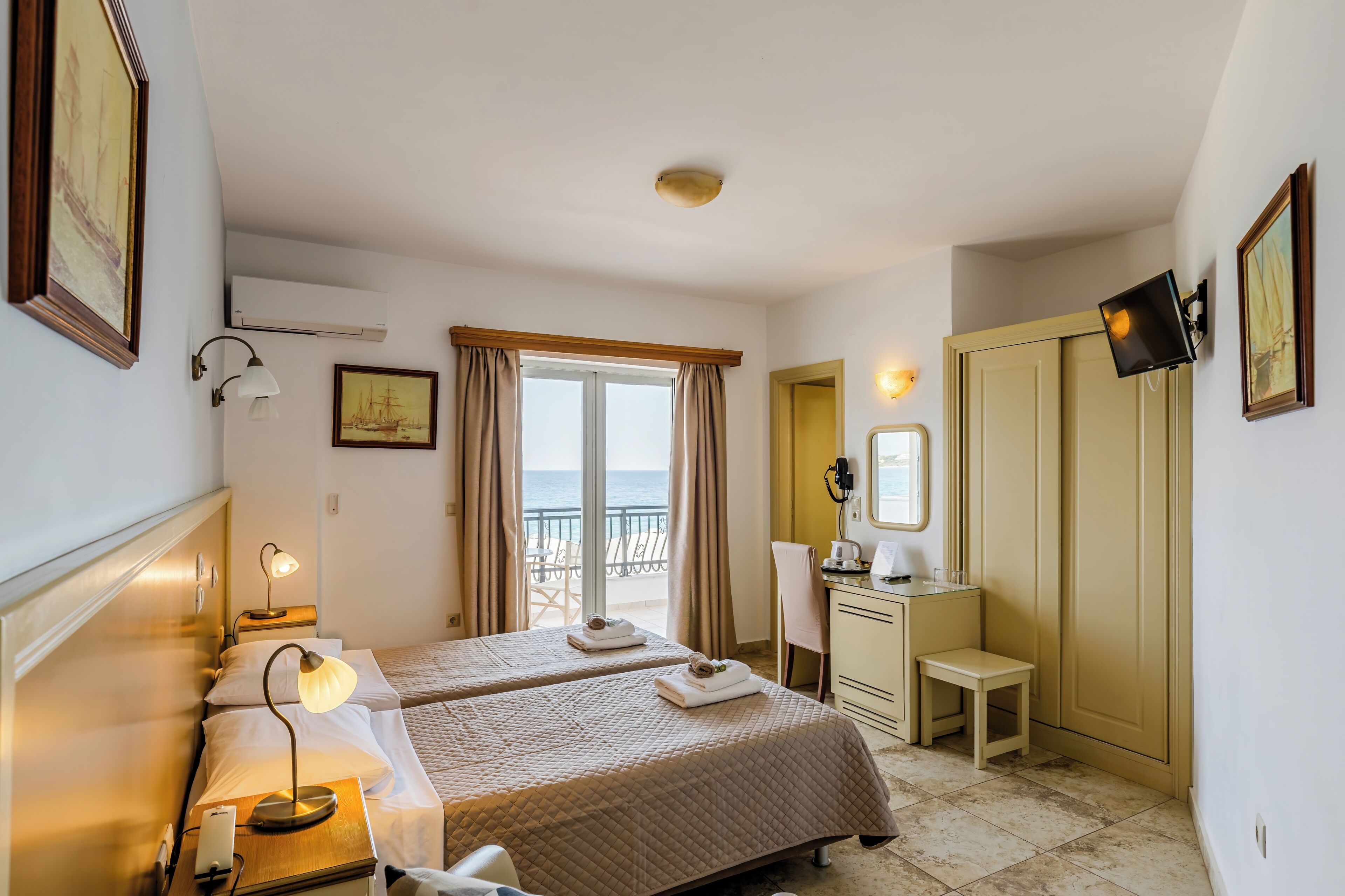 Habitación de hotel con dos camas, un escritorio, una silla, un televisor y un balcón con vista al mar.
