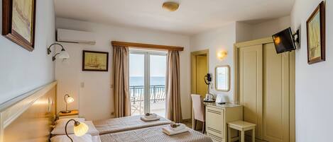 Habitación de hotel con dos camas, un escritorio, una silla, un televisor y un balcón con vista al mar.