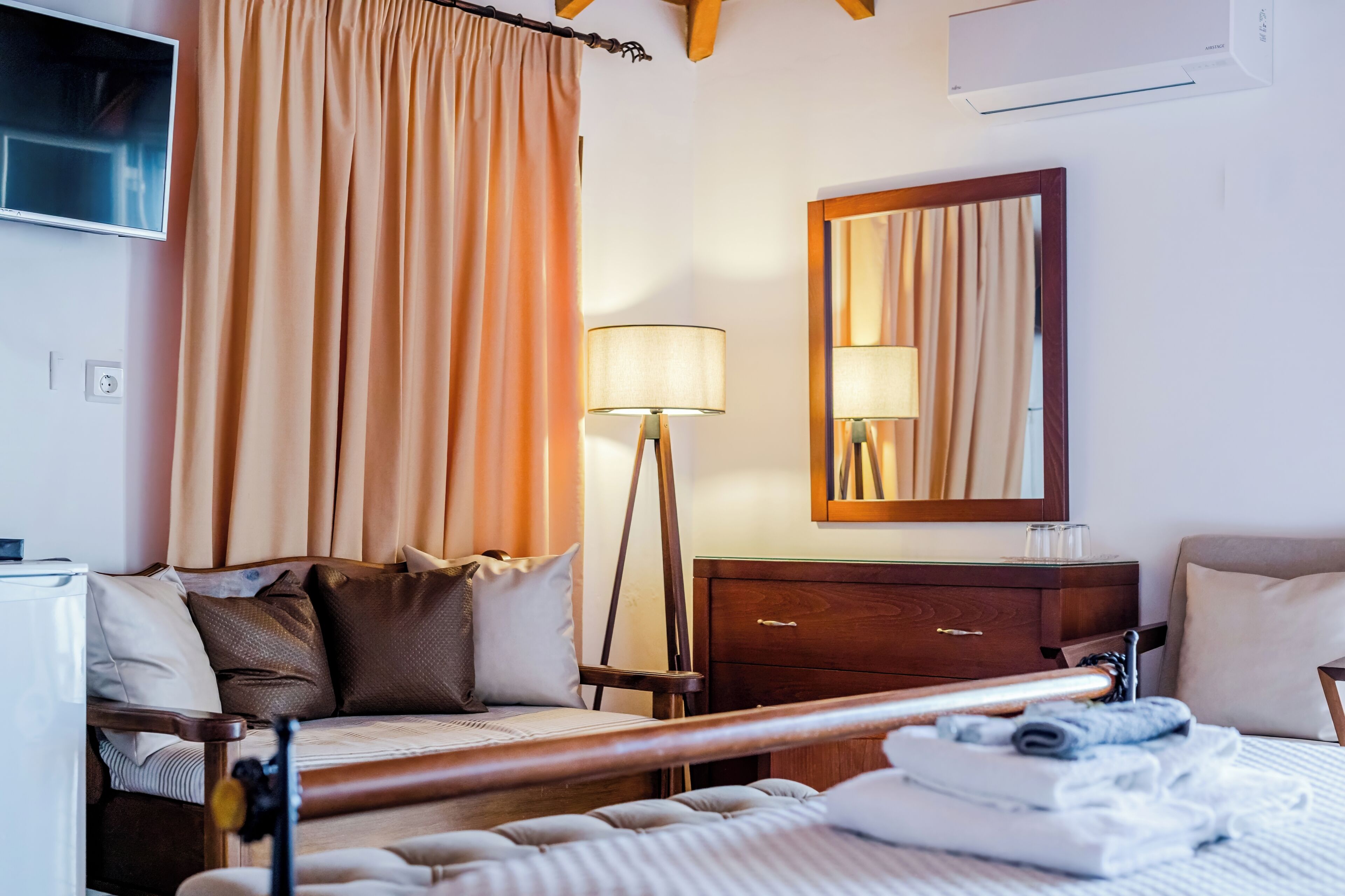 A hotel room with a bed, bedside table, lamp, mirror, and a TV on the wall.
