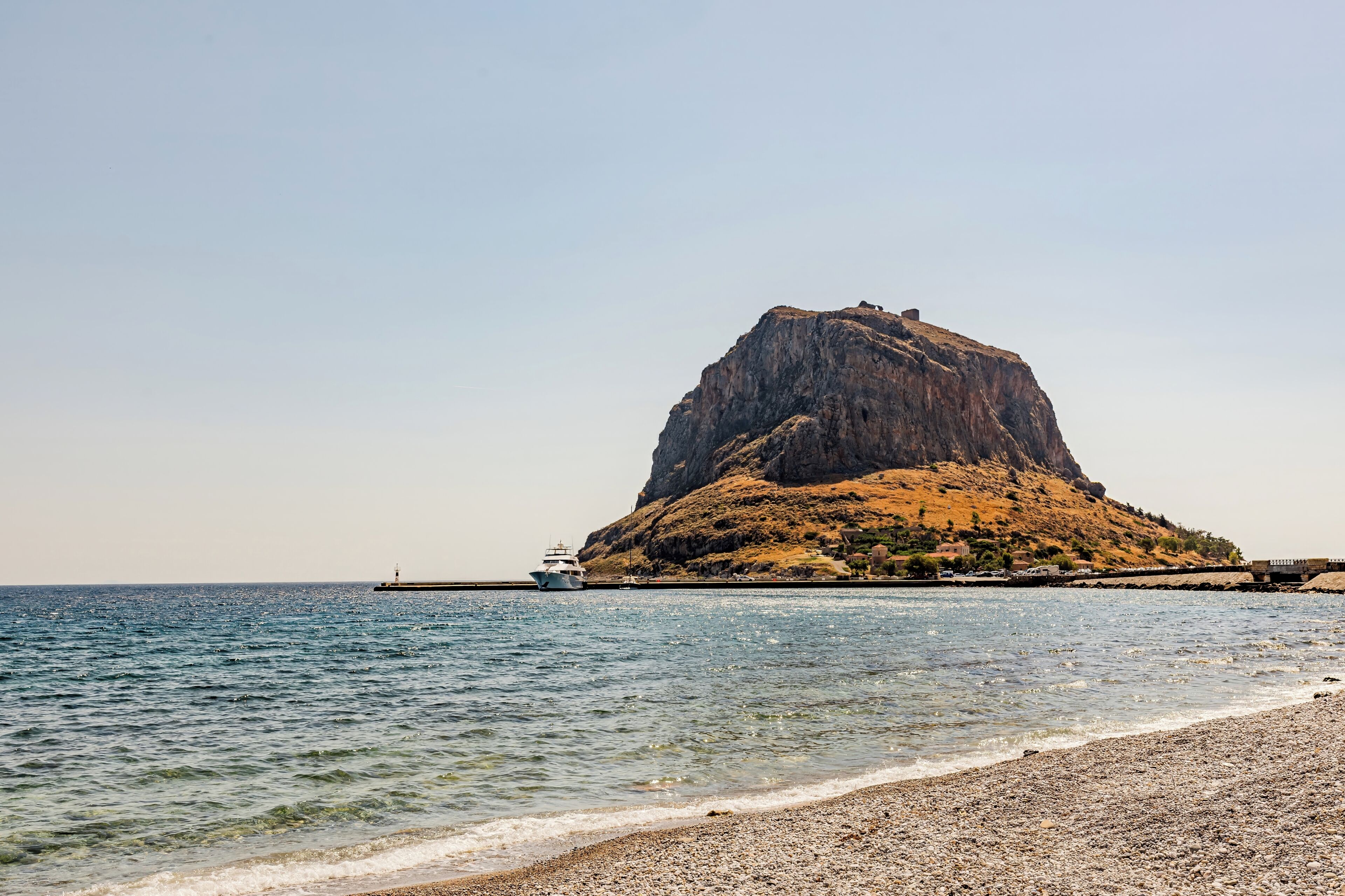 Una illa rocosa amb cel serè, una embarcació a l'aigua i una platja al primer pla.