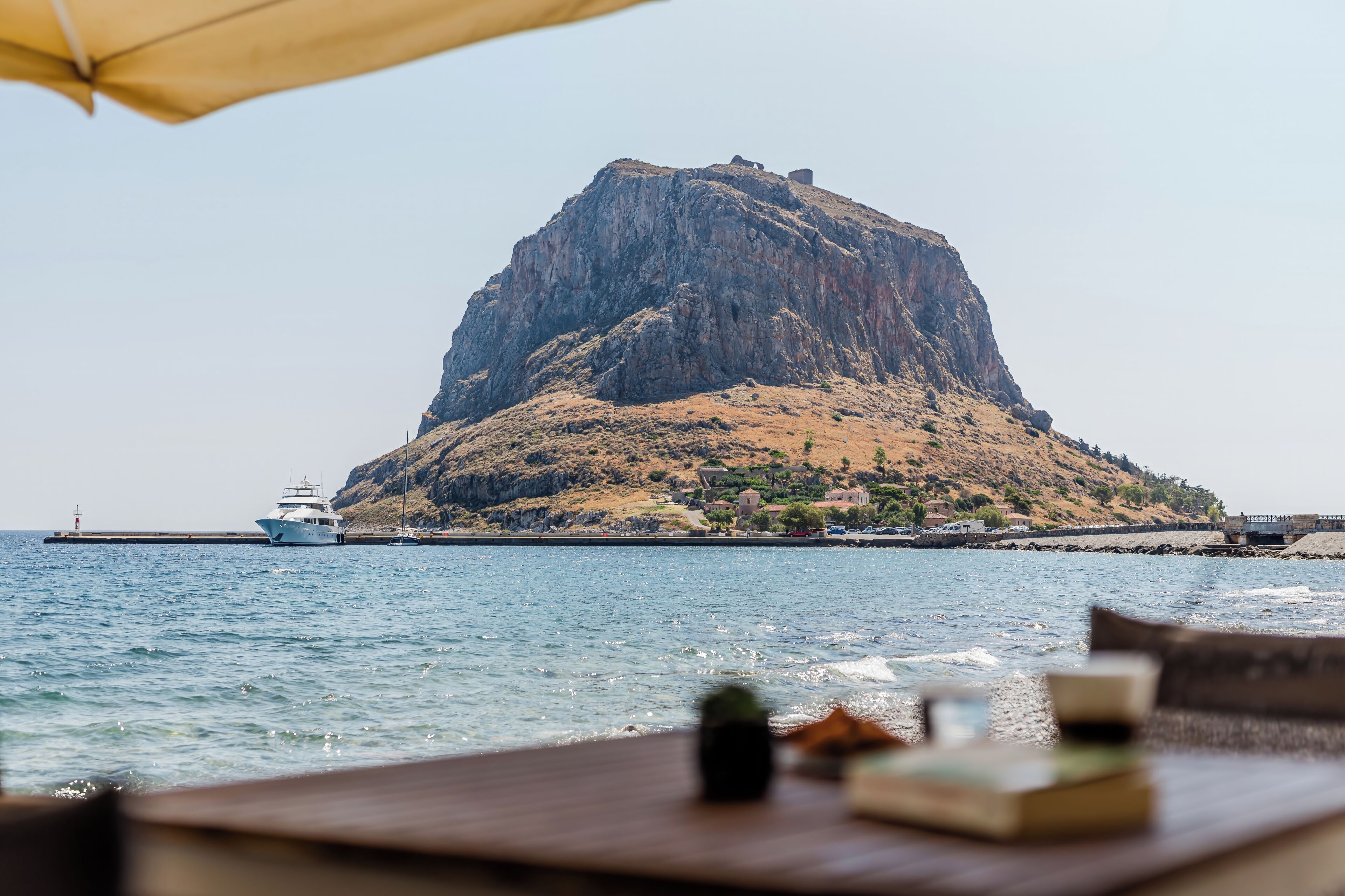 A coastal view with a prominent rocky hill, a pier, and a boat.