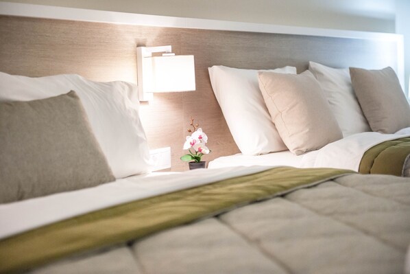Una cama bien hecha con una manta verde, una mesita de noche con una lámpara y una pequeña planta en maceta.