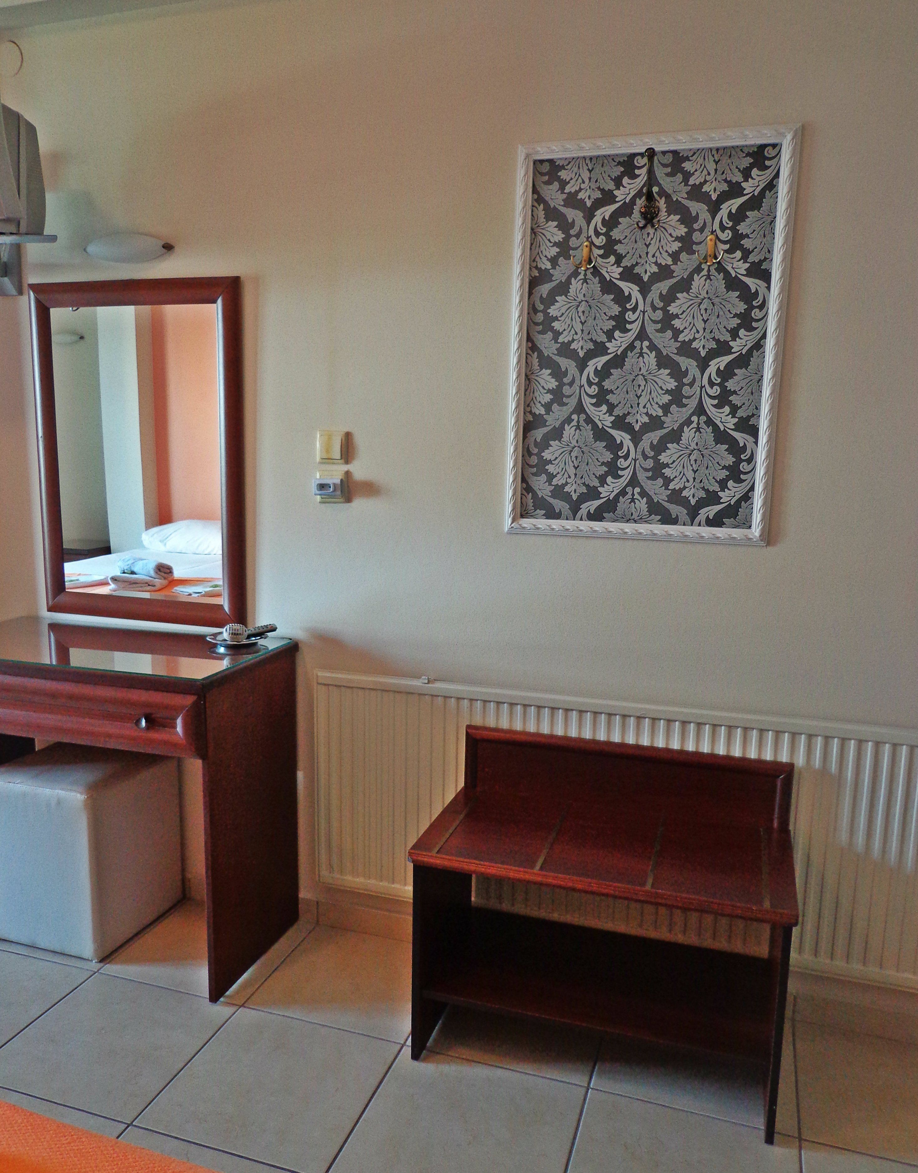 Une chambre d’hôtel avec un bureau en bois, un miroir, un banc, un radiateur et un mur à motifs.