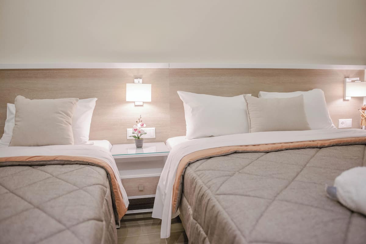 Ein Hotelzimmer mit zwei Betten, einem Nachttisch mit Lampe und einem kleinen Tisch mit Blumenvase.