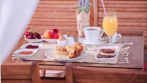 A breakfast setup on a wooden table with a cup of coffee, a glass of orange juice, and various pastries and fruits.