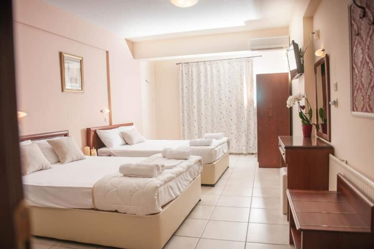 Ein Hotelzimmer mit zwei Betten, einem hölzernen Schminktisch, einem Spiegel und einem Fenster mit Vorhängen.