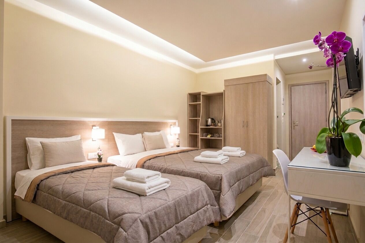A hotel room with two beds, a desk, a wardrobe, and a potted plant.