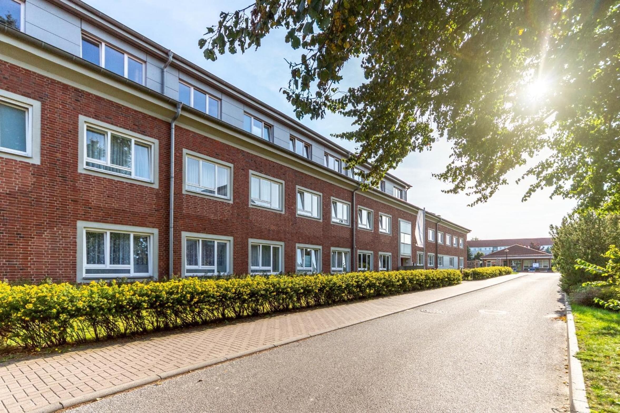 A row of red brick apartment buildings with uniform windows and a paved road in front.