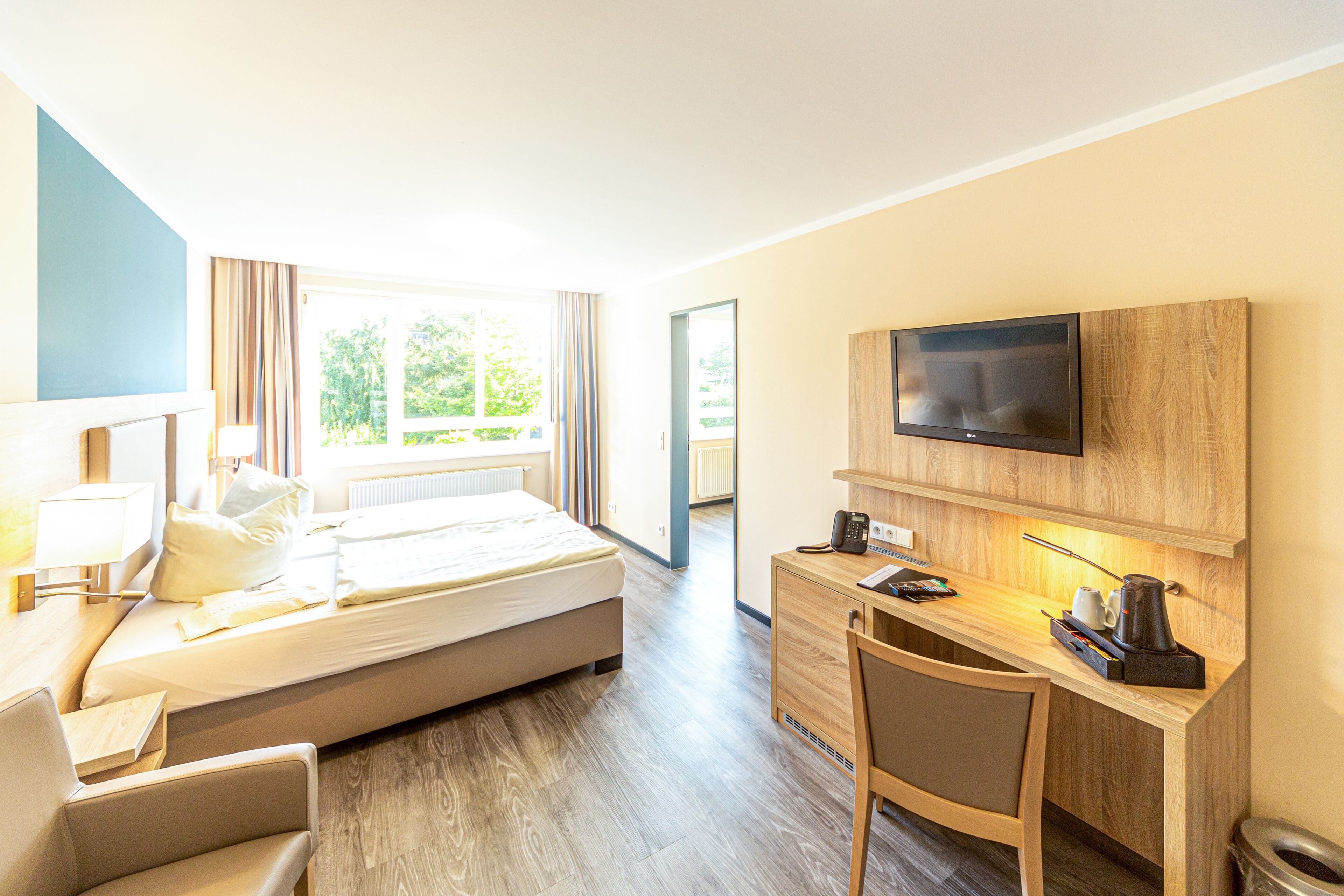 Habitación de hotel con cama, escritorio con computadora, televisor y ventana con cortinas.