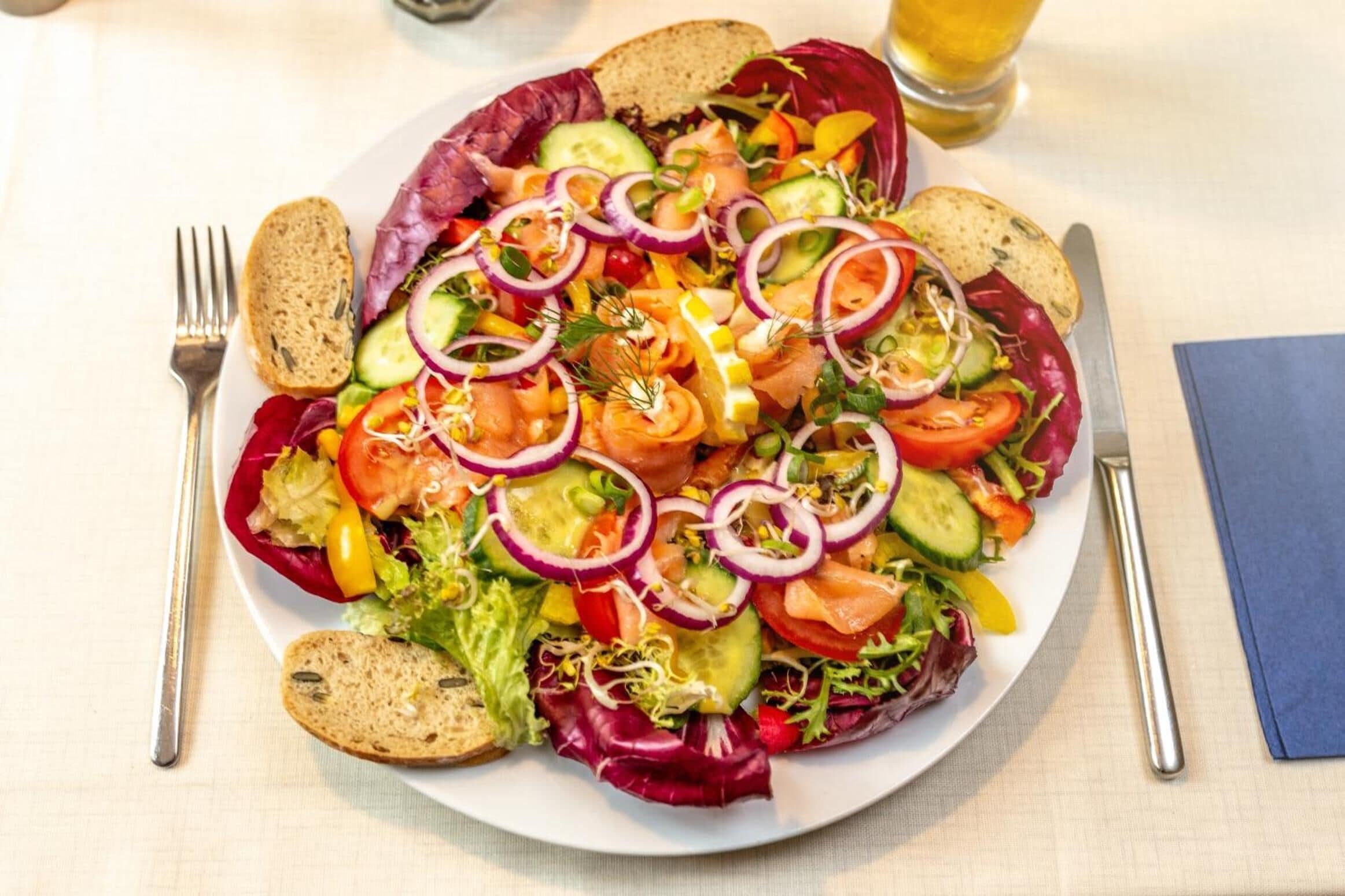 A plate of salad with various vegetables and slices of salmon, accompanied by slices of bread.