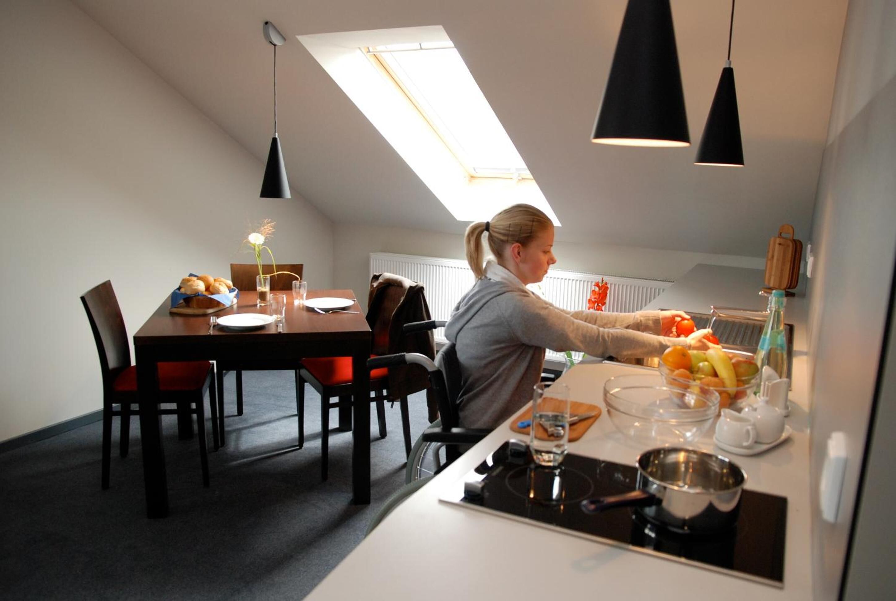 A modern kitchen with a skylight, a dining area with a table set for two, and a person preparing food.