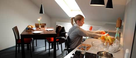 A modern kitchen with a skylight, a dining area with a table set for two, and a person preparing food.