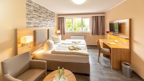 Habitación de hotel con cama, escritorio, silla, televisor y ventana con cortinas.