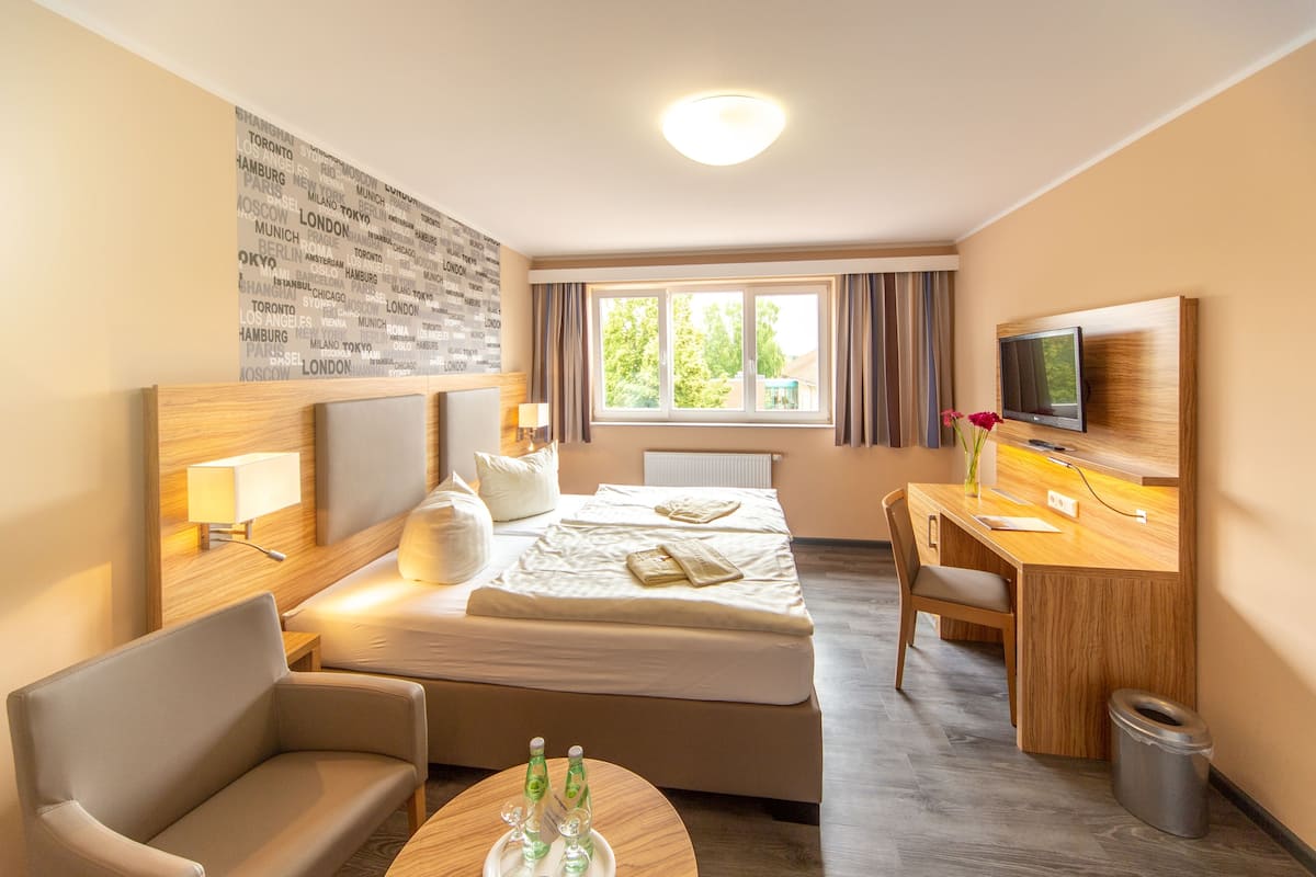 A hotel room with a bed, a desk, a chair, a TV, and a window with curtains.